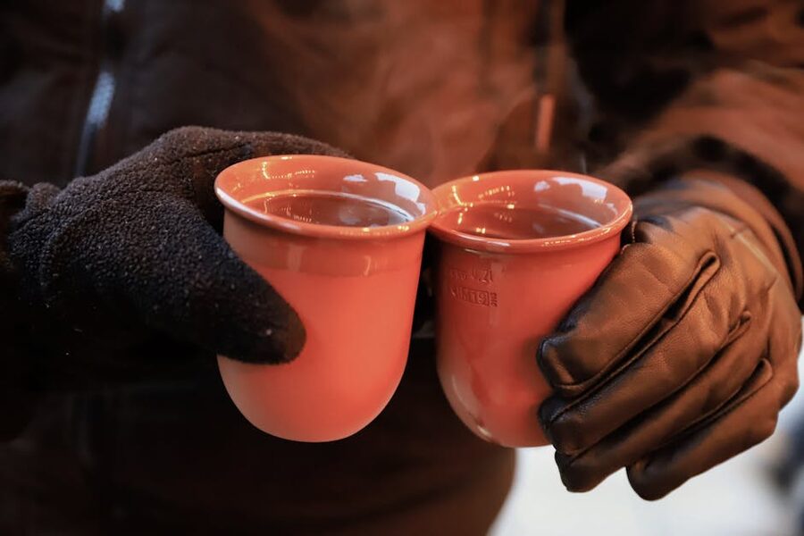 Two hands clinking warm Glühwein mugs at a German Christmas market