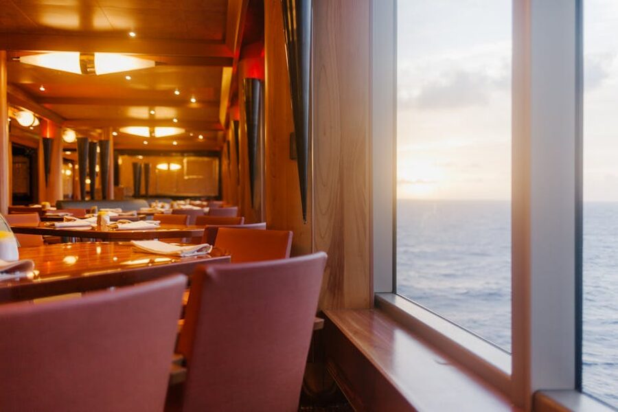 An empty wooden dining table set with white cloth on a luxury ship deck at sunset