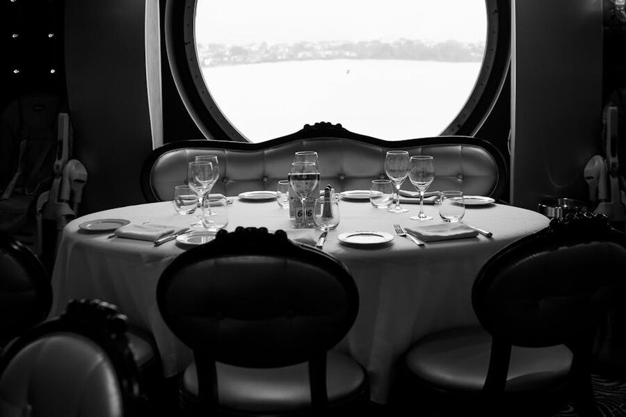 A set table by a round porthole window inside a cruise ship dining room