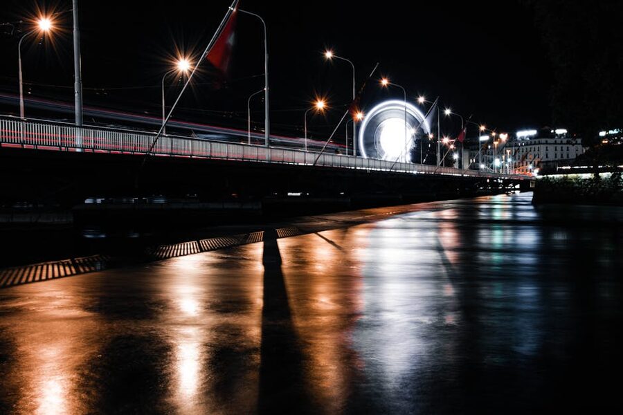 Geneva bridge at night with illuminated ferris wheel reflected in Lake Geneva